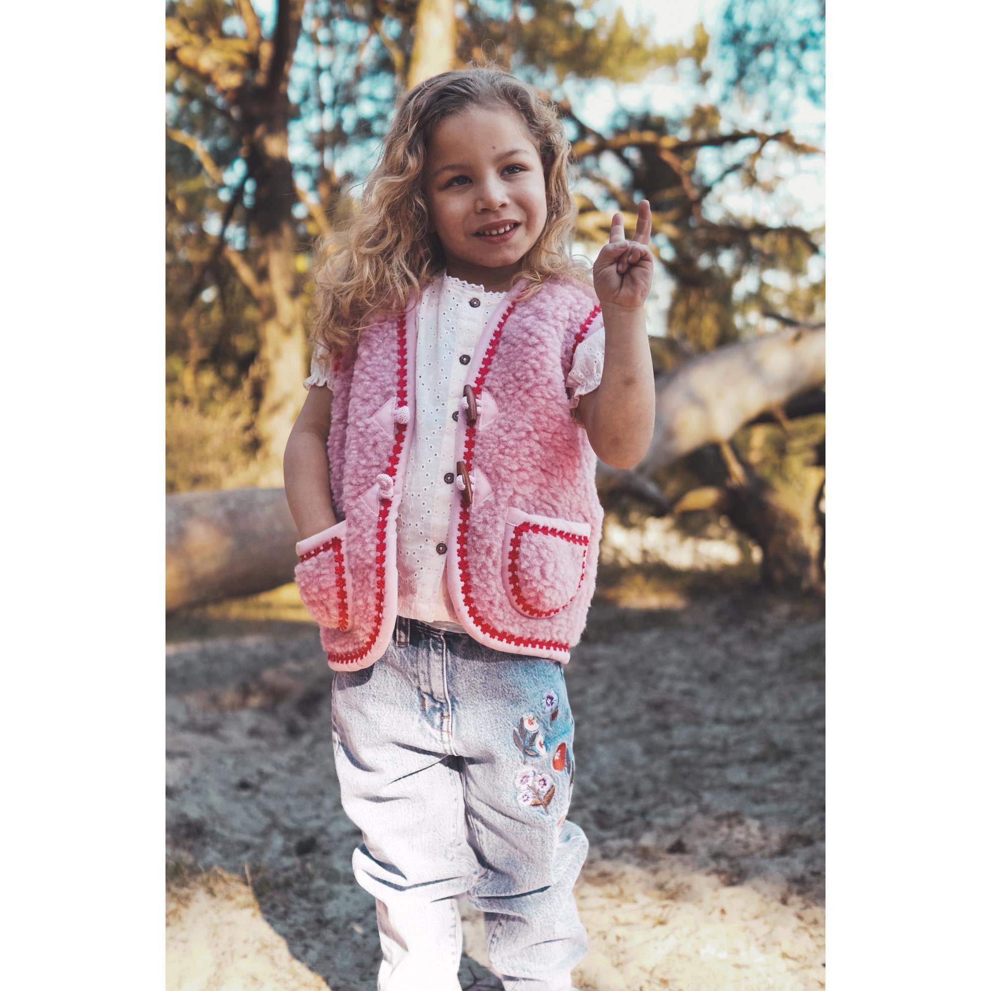 Young girl wearing a pink wool bodywarmer outdoors with trees in the background