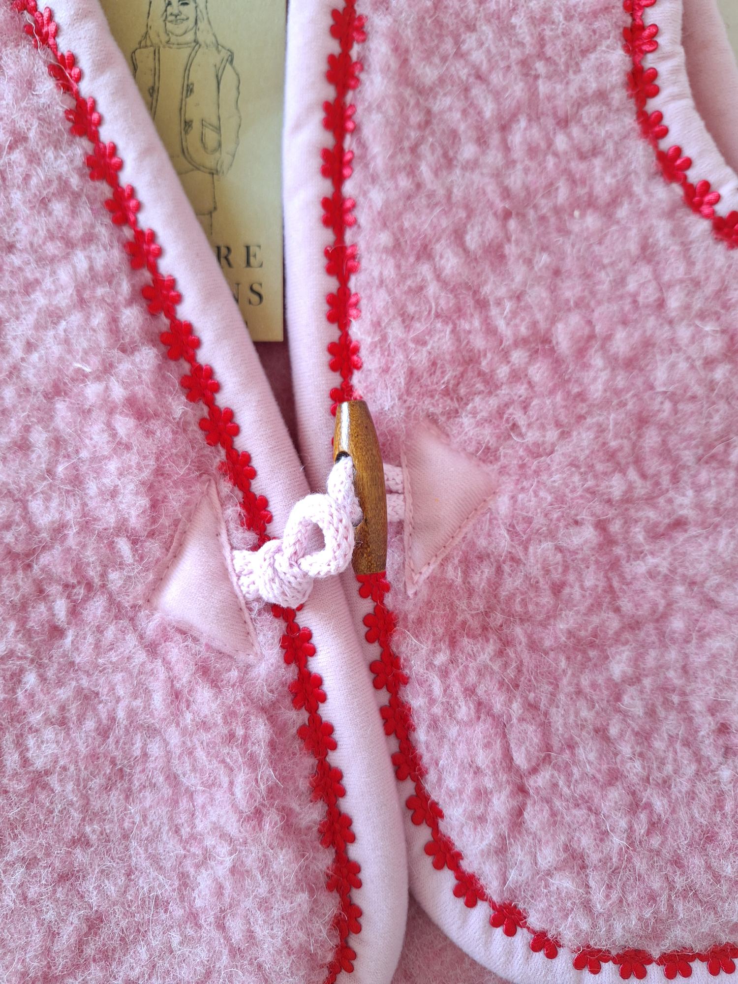 Close-up of a pink wool bodywarmer with buckle tie open on front with red floral trim