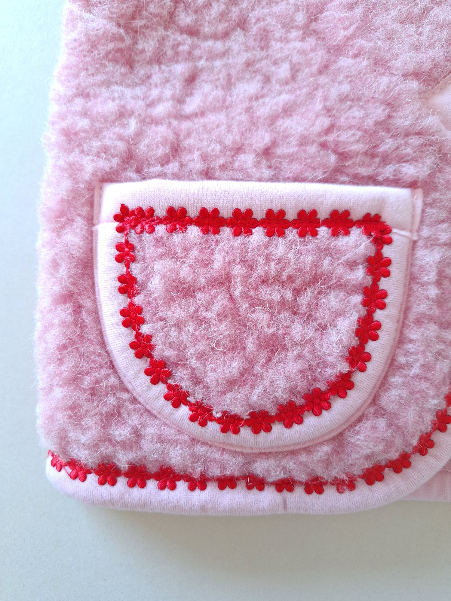 Pink wool bodywarmer pocket with red floral trim on a cream background