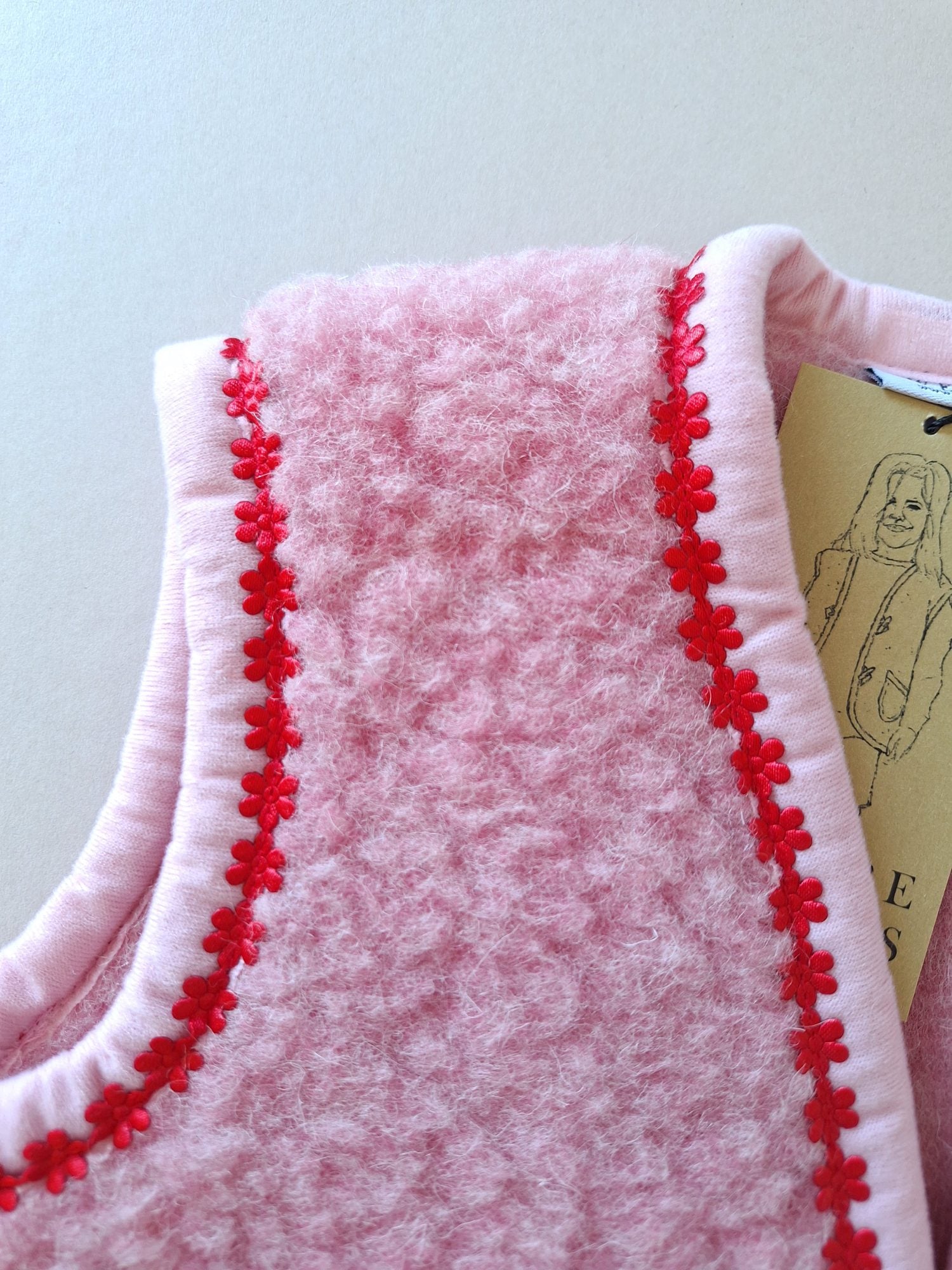Shoulder detail of pink wool bodywarmer with red floral trim on a cream background