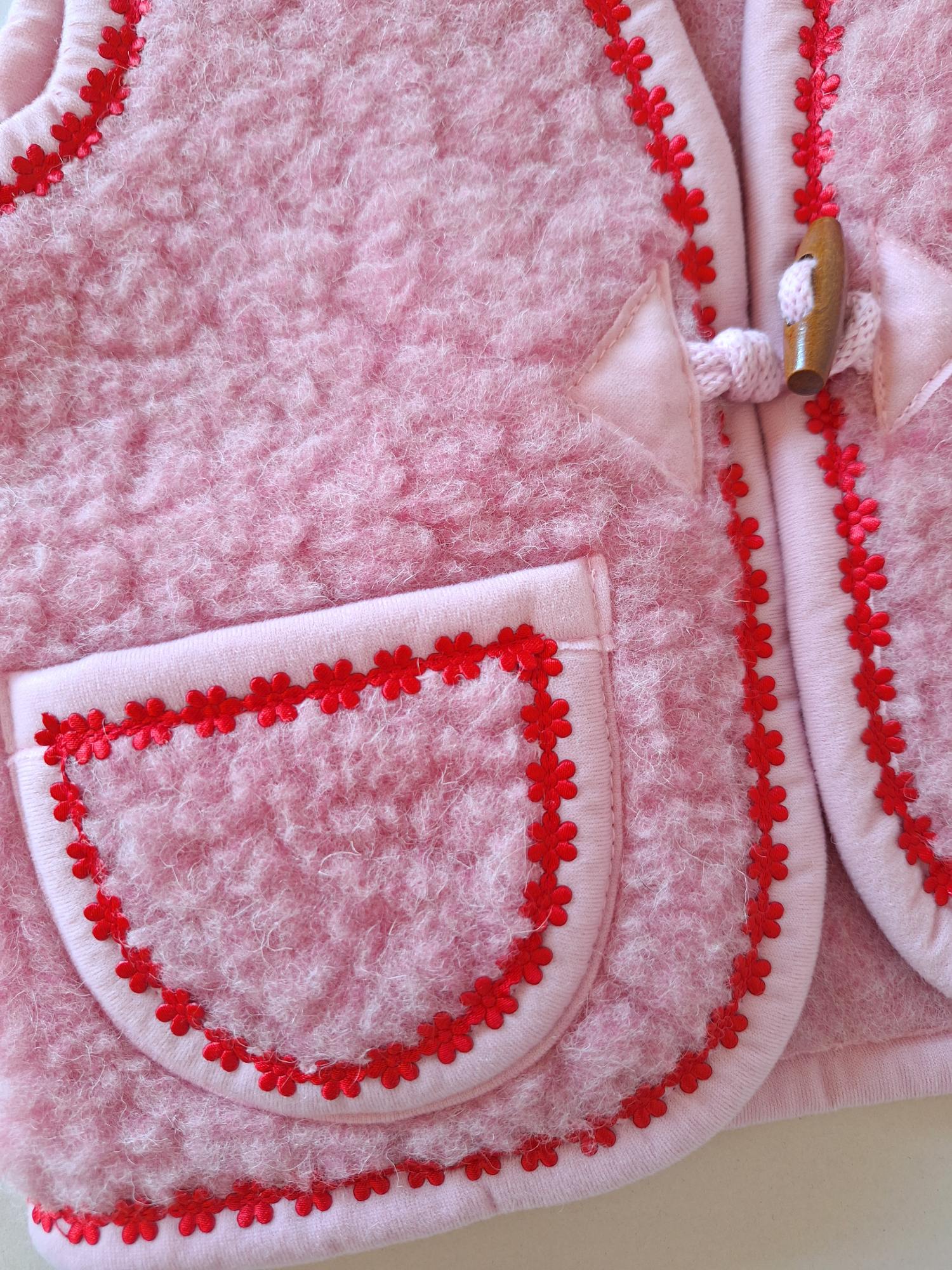 Close-up of pocket on a pink merino wool fabric with red flower trim on a cream background