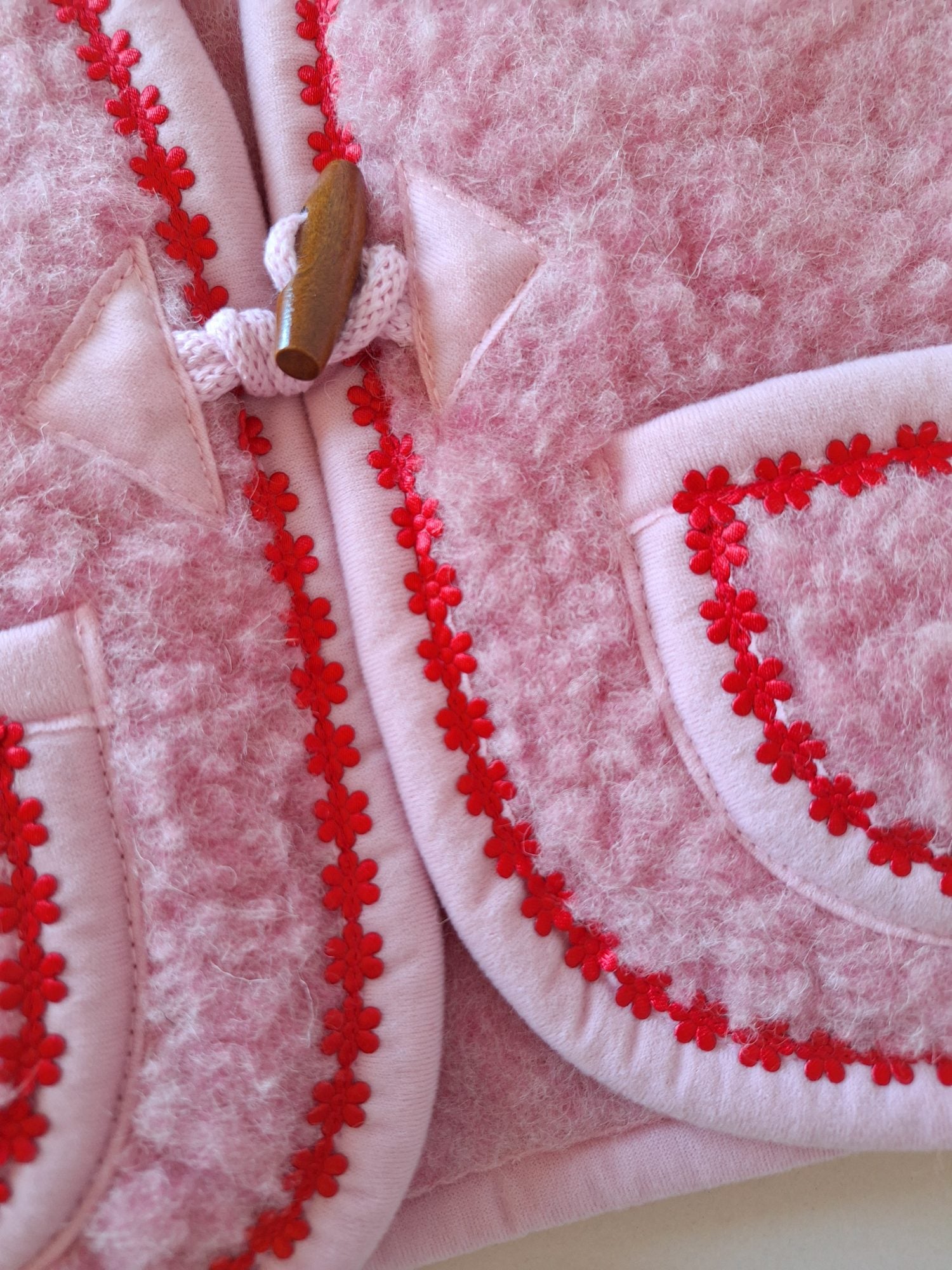 Close-up of wooden buckle tie on a pink wool bodywarmer with red floral trim