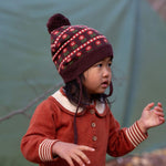Child wearing a patterned knit hat and ginger knitted dress against a green background