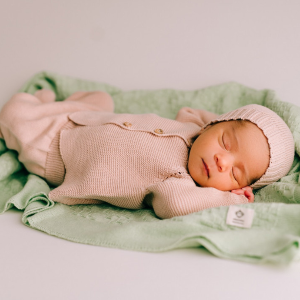 Newborn baby in pink knitted outfit sleeping on a green blanket