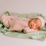 Newborn baby in pink knitted outfit sleeping on a green blanket