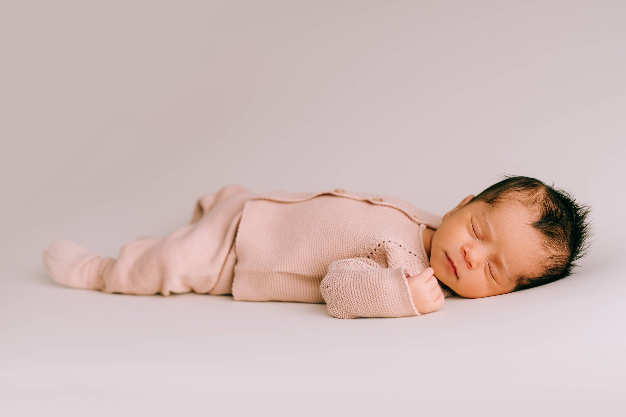 Newborn baby in pink knitted two-piece set lying on a light grey background