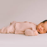 Newborn baby in pink knitted two-piece set lying on a light grey background