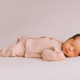 Newborn baby in pink knitted two-piece set lying on a light grey background