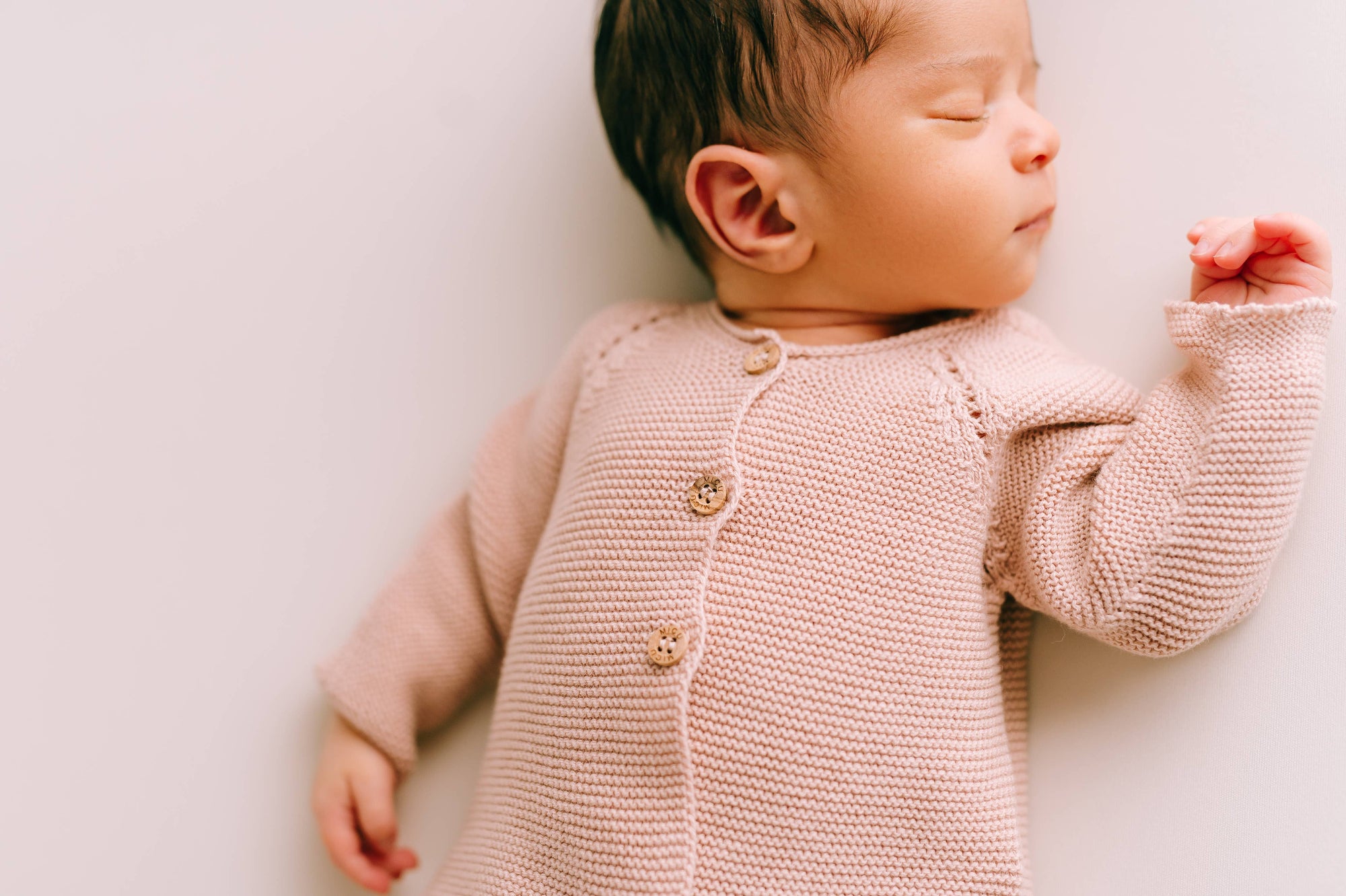 Newborn baby wearing a pink knitted cardigan on a white background
