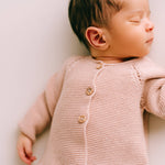 Newborn baby wearing a pink knitted cardigan on a white background