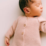 Newborn baby wearing a pink knitted cardigan on a white background
