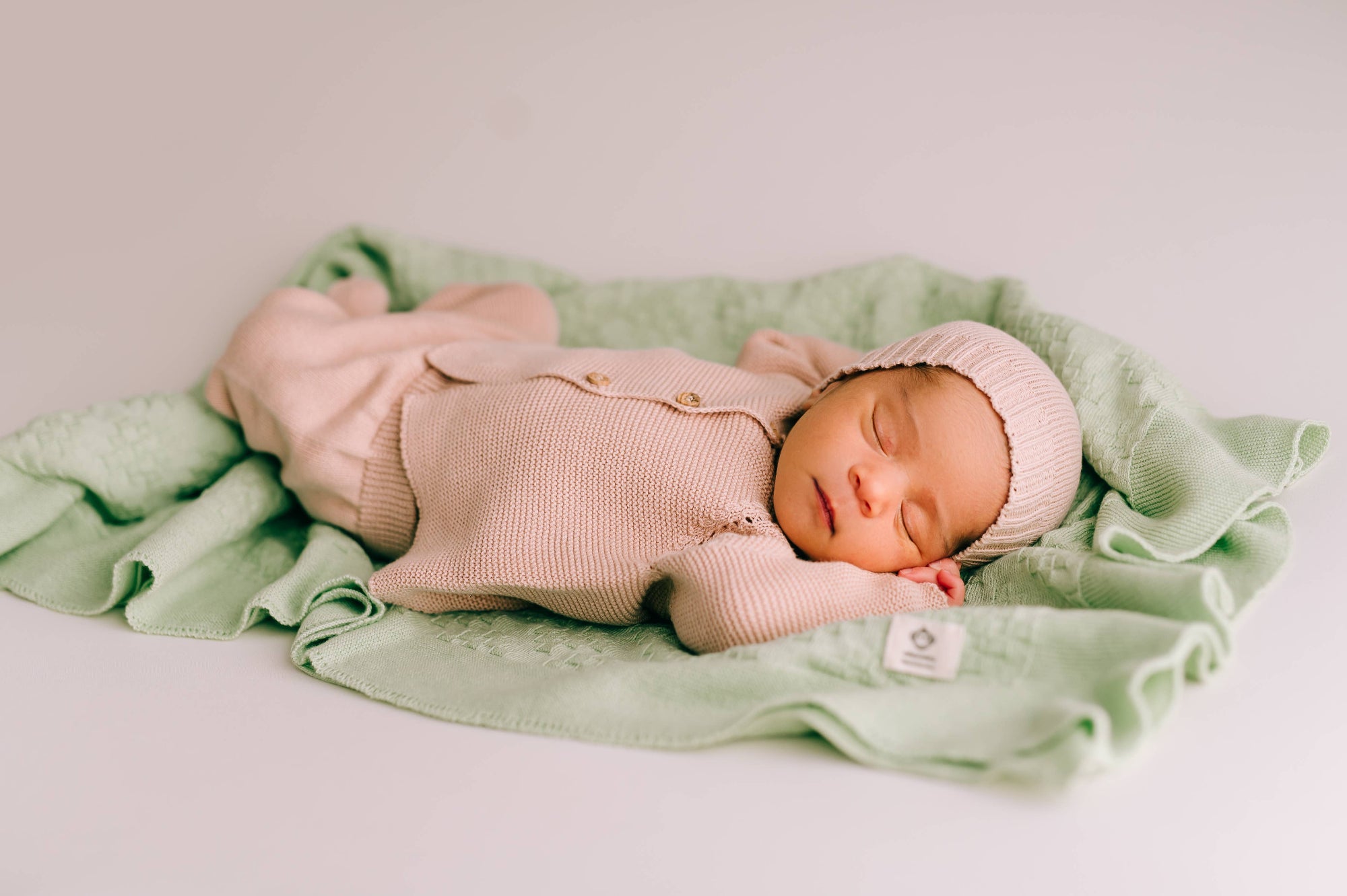Newborn baby in pink knitted outfit and hat lying on a green blanket