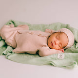 Newborn baby in pink knitted outfit and hat lying on a green blanket