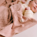 Newborn baby wrapped in a pink knitted blanket with a visible brand tag.