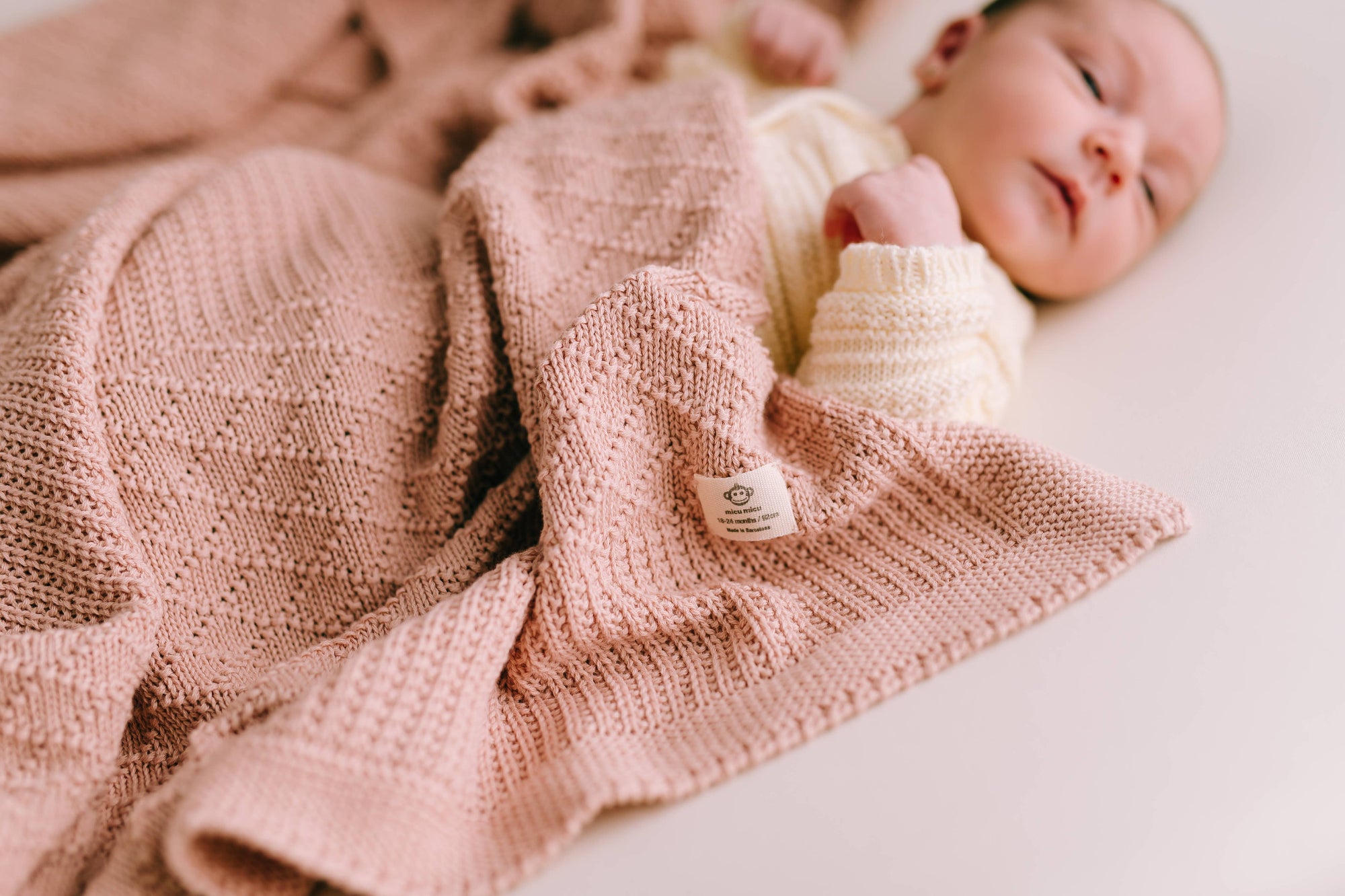 Newborn baby wrapped in a pink knitted blanket with a visible brand tag.