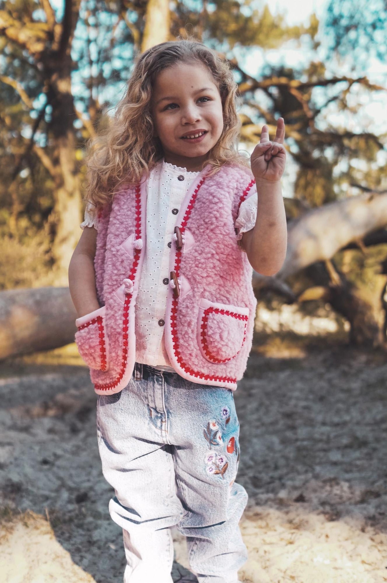 Young girl wearing a pink wool bodywarmer outdoors with trees in the background