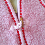 Close-up of a pink wool bodywarmer with buckle tie open on front with red floral trim
