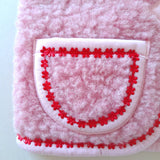 Pink wool bodywarmer pocket with red floral trim on a cream background
