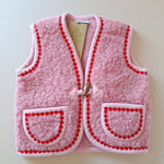 Pink children's wool bodywarmer with red flower trim on a cream background