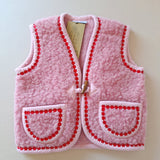 Pink children's wool bodywarmer with red flower trim on a cream background