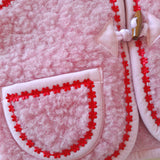 Close-up of pocket on a pink merino wool fabric with red flower trim on a cream background